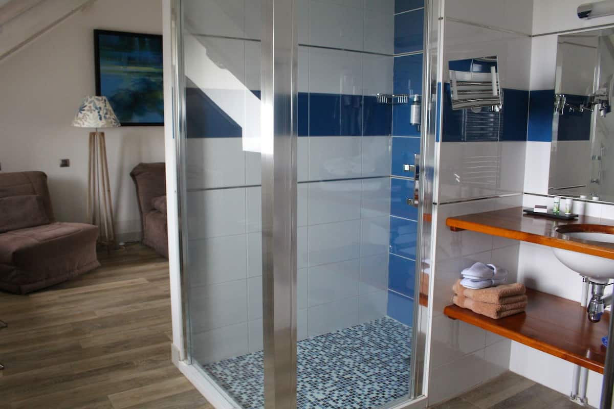 Un baño moderno con ducha envuelta en vidrio, tocador de madera y pared con azulejos azules y blancos.