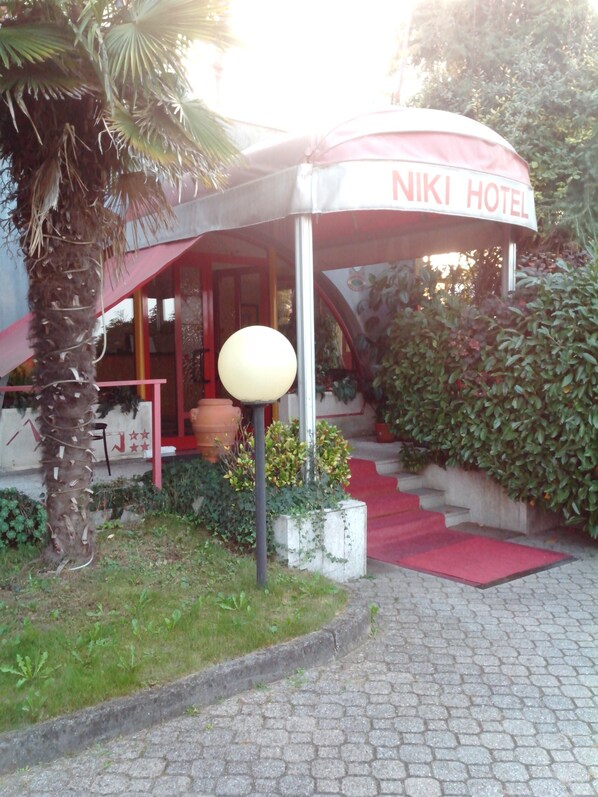 A hotel entrance with a red awning, a lamp post, and a staircase leading to the entrance.