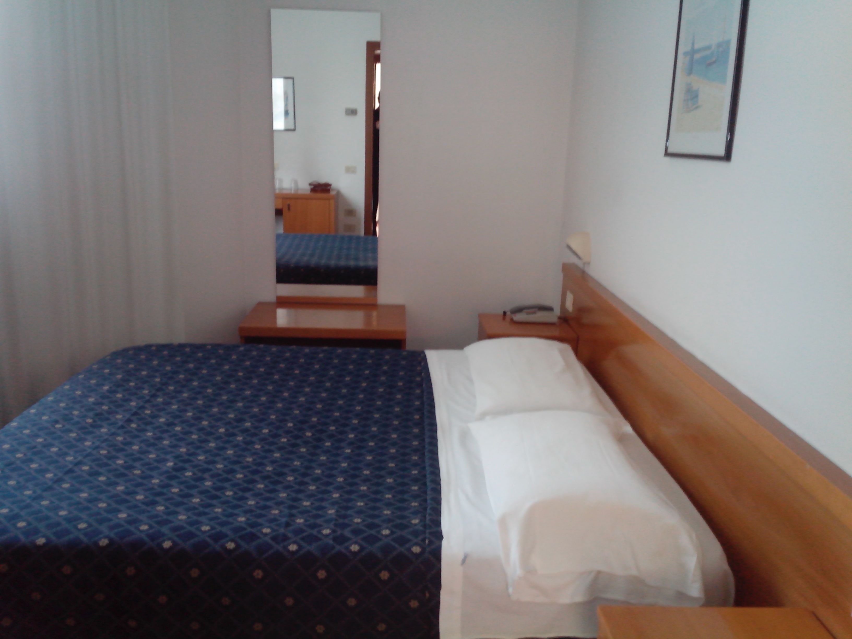 A hotel room with a bed, a nightstand, a mirror, and a framed picture on the wall.