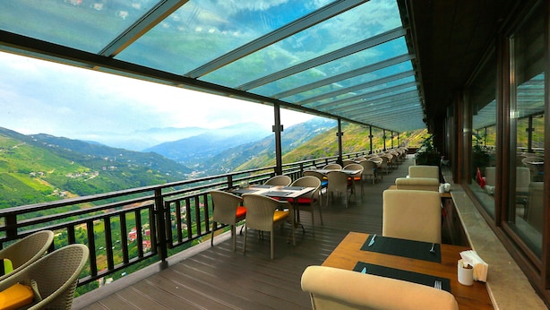 Restaurante com área externa e mesas apreciando uma paisagem montanhosa.