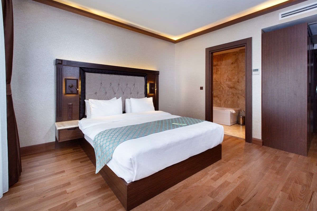 A modern hotel room with a large bed, wooden flooring, and a built-in wardrobe.
