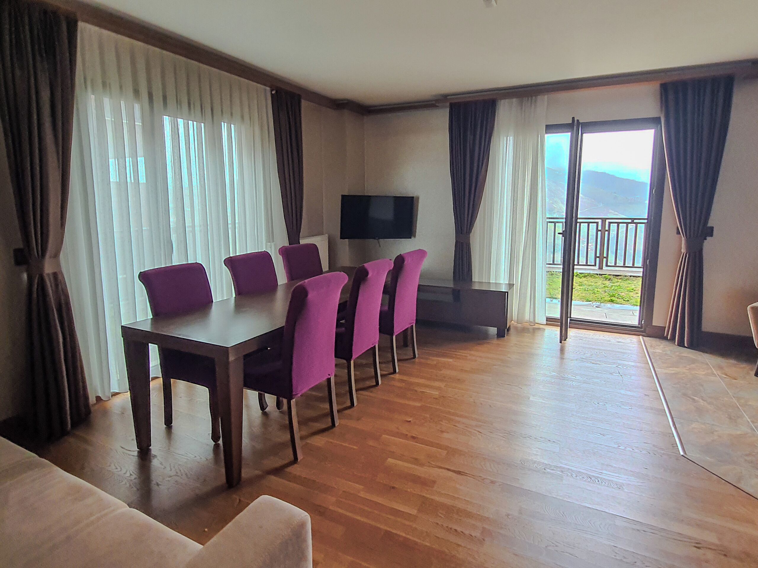 Ein Essbereich mit Tisch und Stühlen, einem Fernseher und einem Balkon mit Blick.