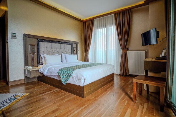 A hotel room with a wooden bed, a bedside table with a lamp, a TV, and a window with curtains.