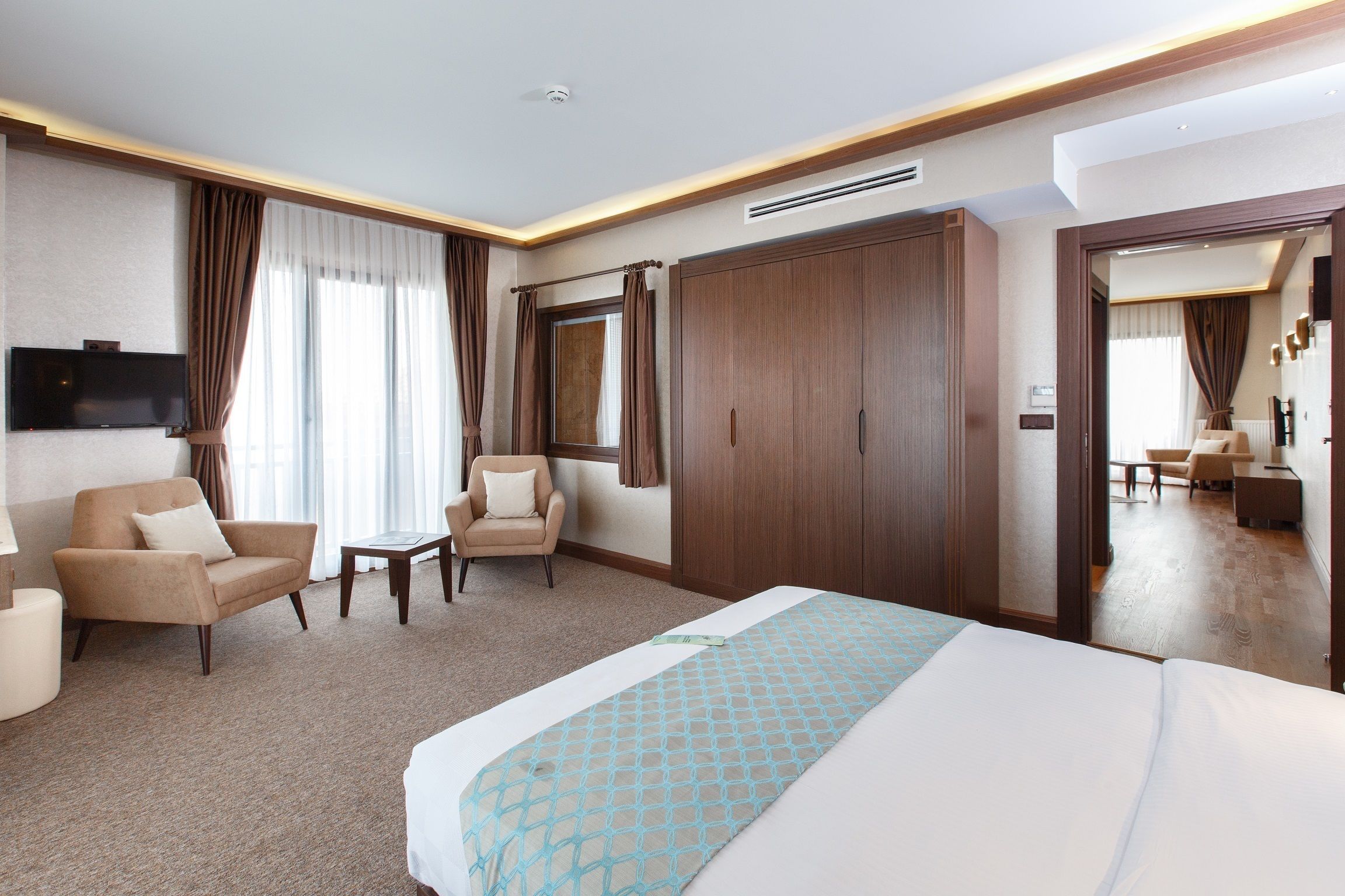 A hotel room with a large bed, a sofa, a chair, a TV, and a wardrobe.