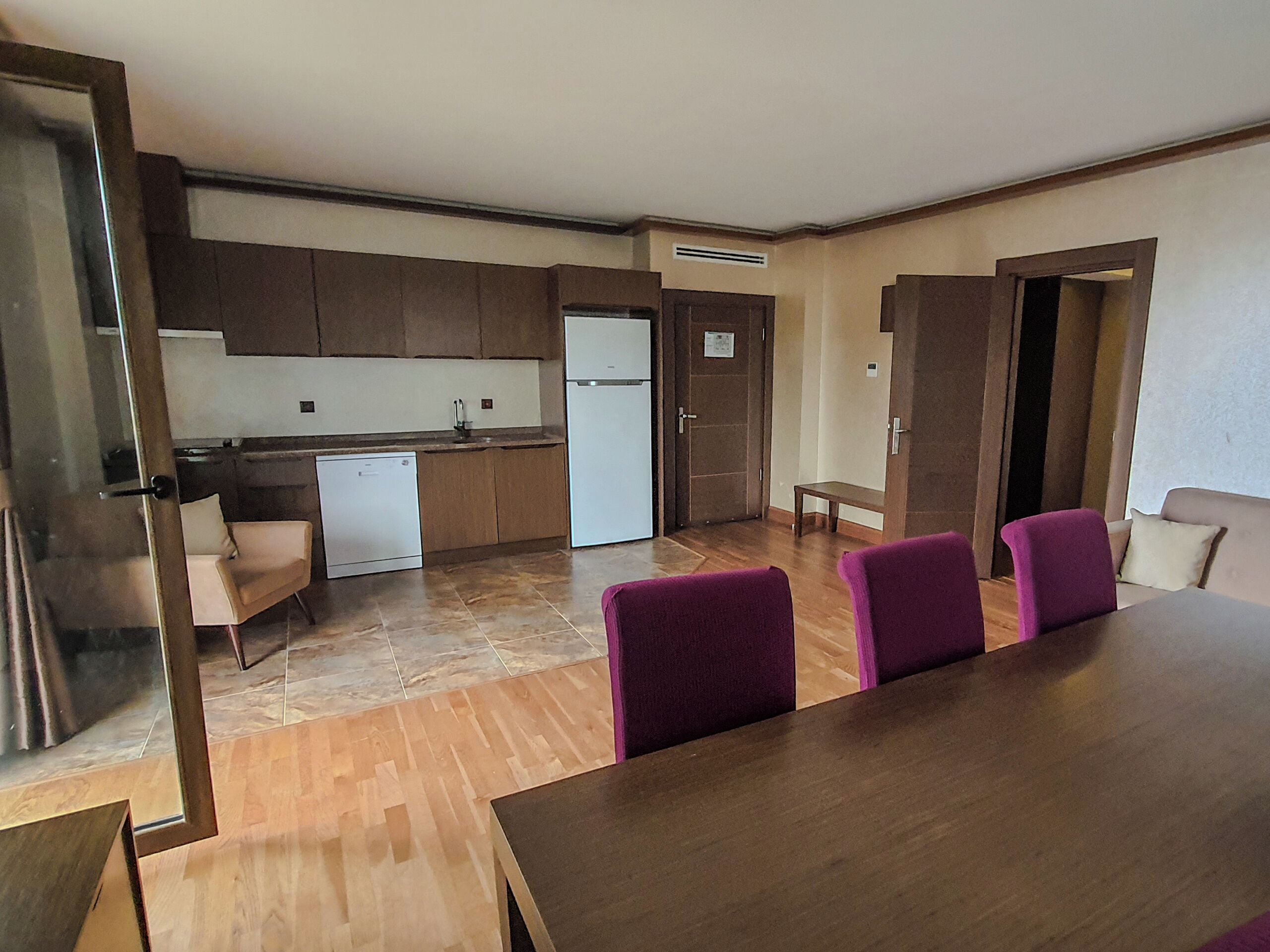 Una cucina moderna con lavastoviglie, frigorifero e mobili in legno. C'è un'area pranzo con tavolo e sedie viola.