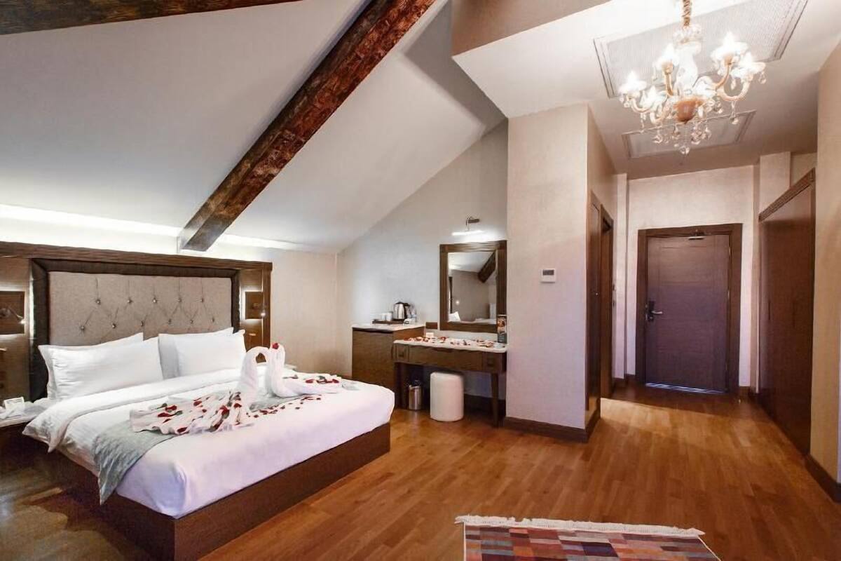 A hotel room with a bed, a desk, a mirror, and a chandelier.
