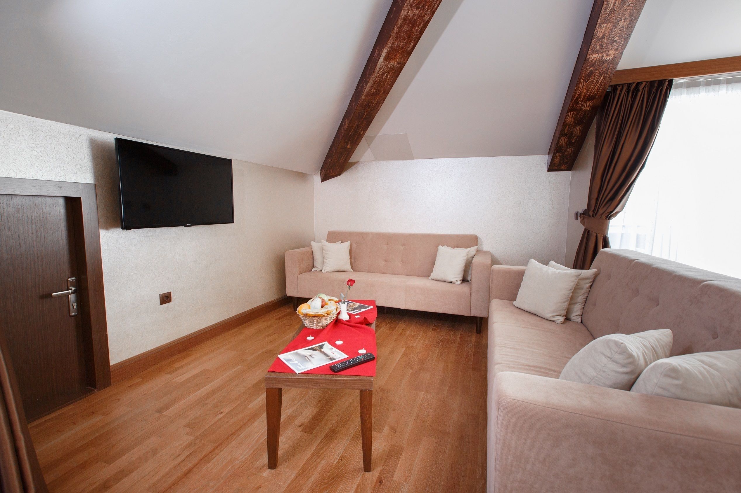 A living room with a wooden floor, a sofa, a television mounted on the wall, and a table with a basket and remote control.