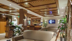 Uma área de recepção de hotel com balcão, espaço para sentar e uma tela de televisão.