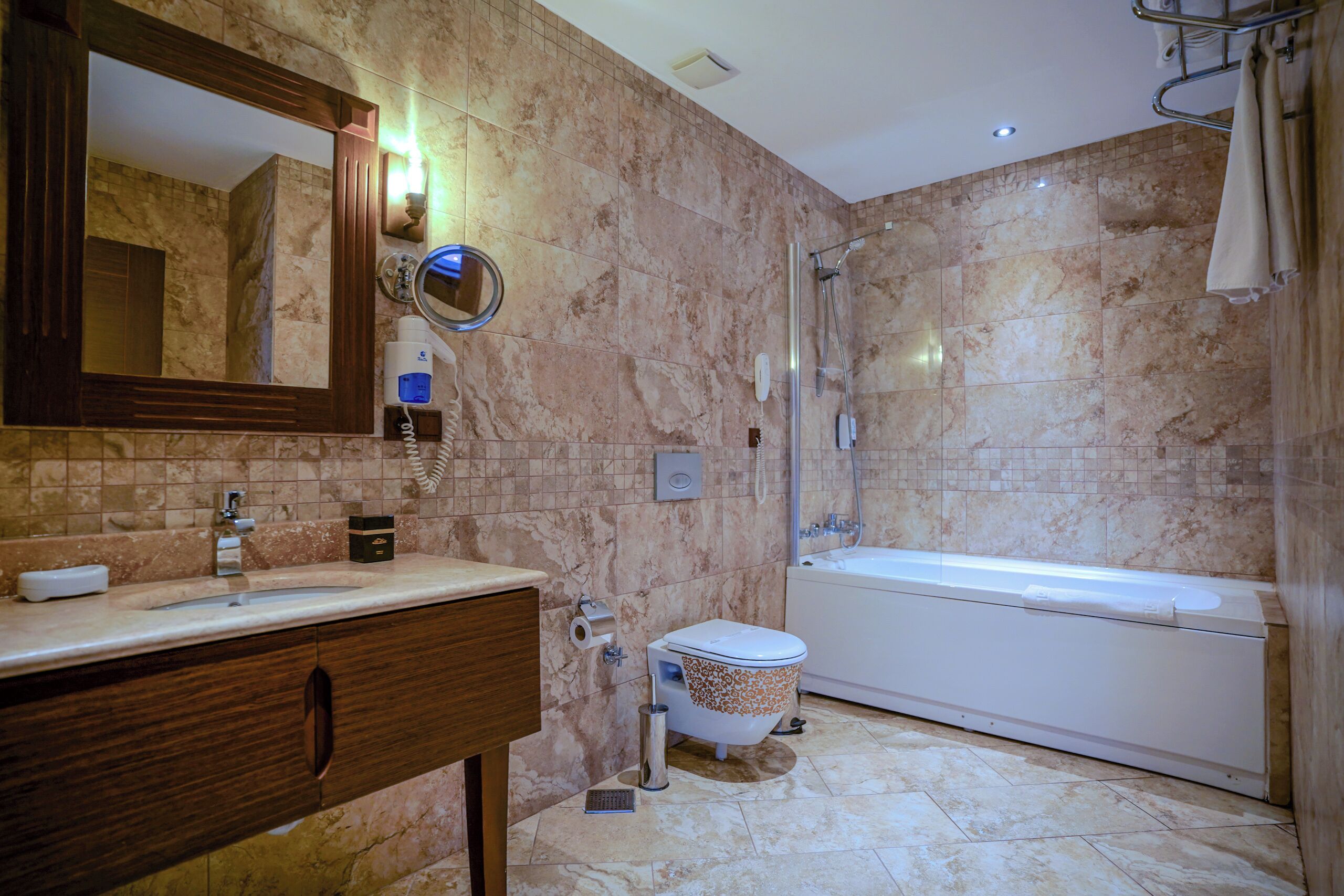 A bathroom with a marble wall, a sink with a mirror, a toilet, and a bathtub.