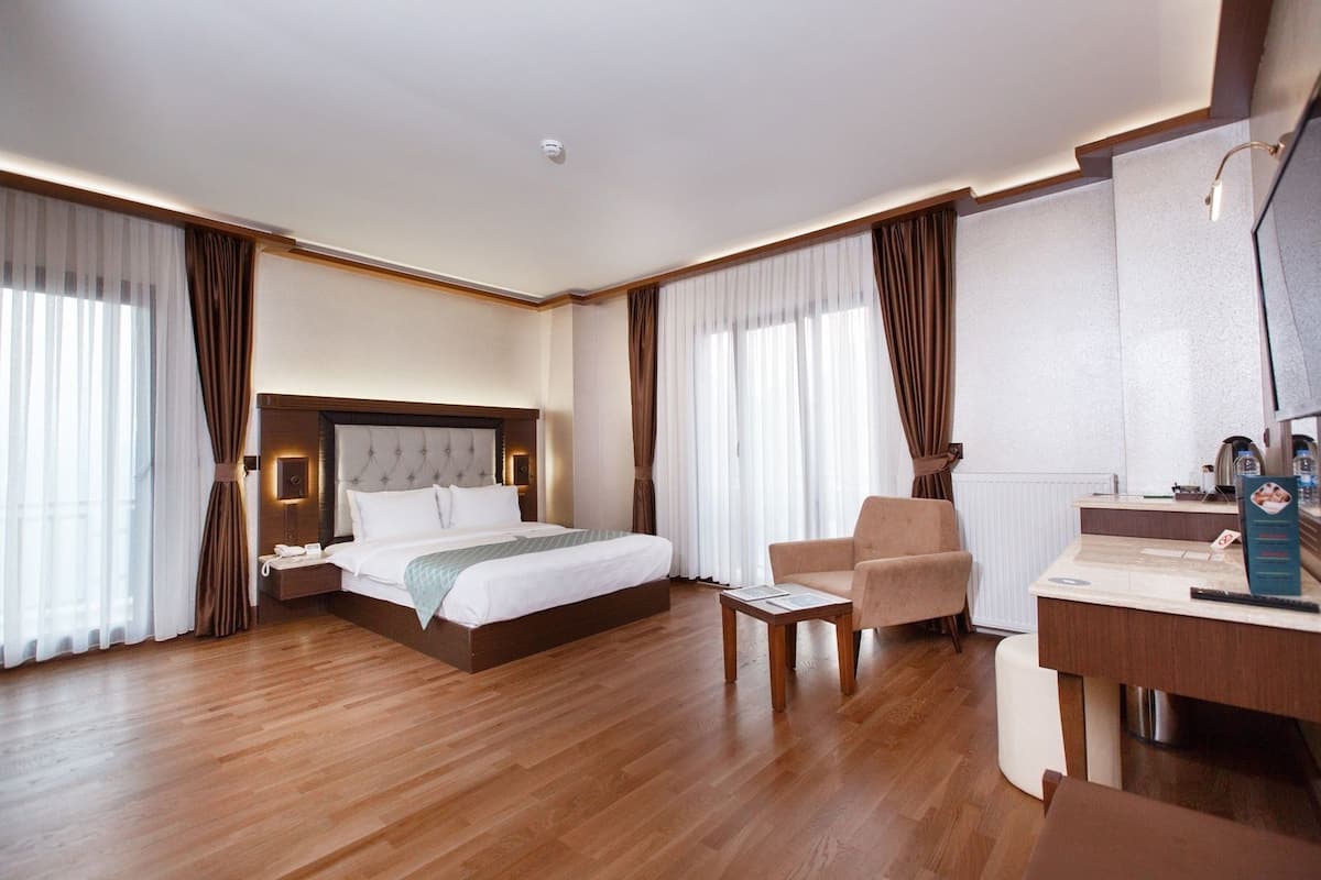 A hotel room with a large bed, a desk, a chair, and a bathroom area.