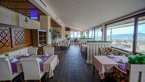 Um restaurante com mesas postas para refeições, teto com padrão de madeira e grandes janelas com vista.