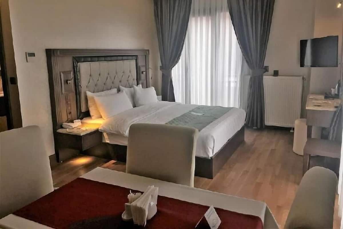 A hotel room with a bed, bedside table, chair, desk, and a TV.