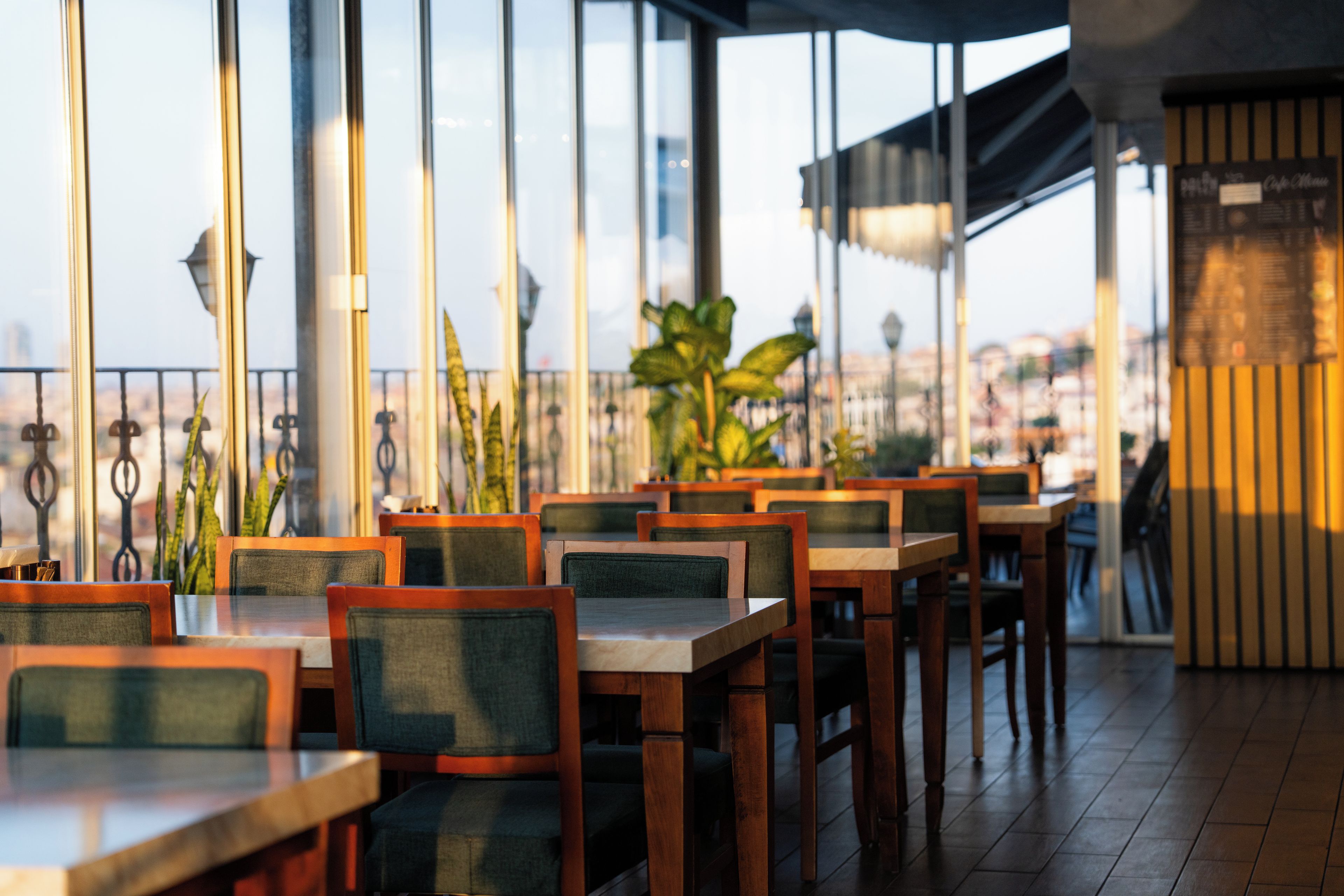 A restaurant with multiple tables and chairs, large windows, and a view of the cityscape.