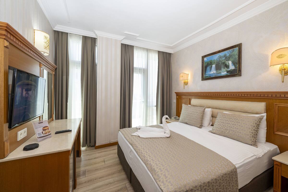 Une chambre d’hôtel avec un lit, une télévision, un bureau et un tableau au mur.