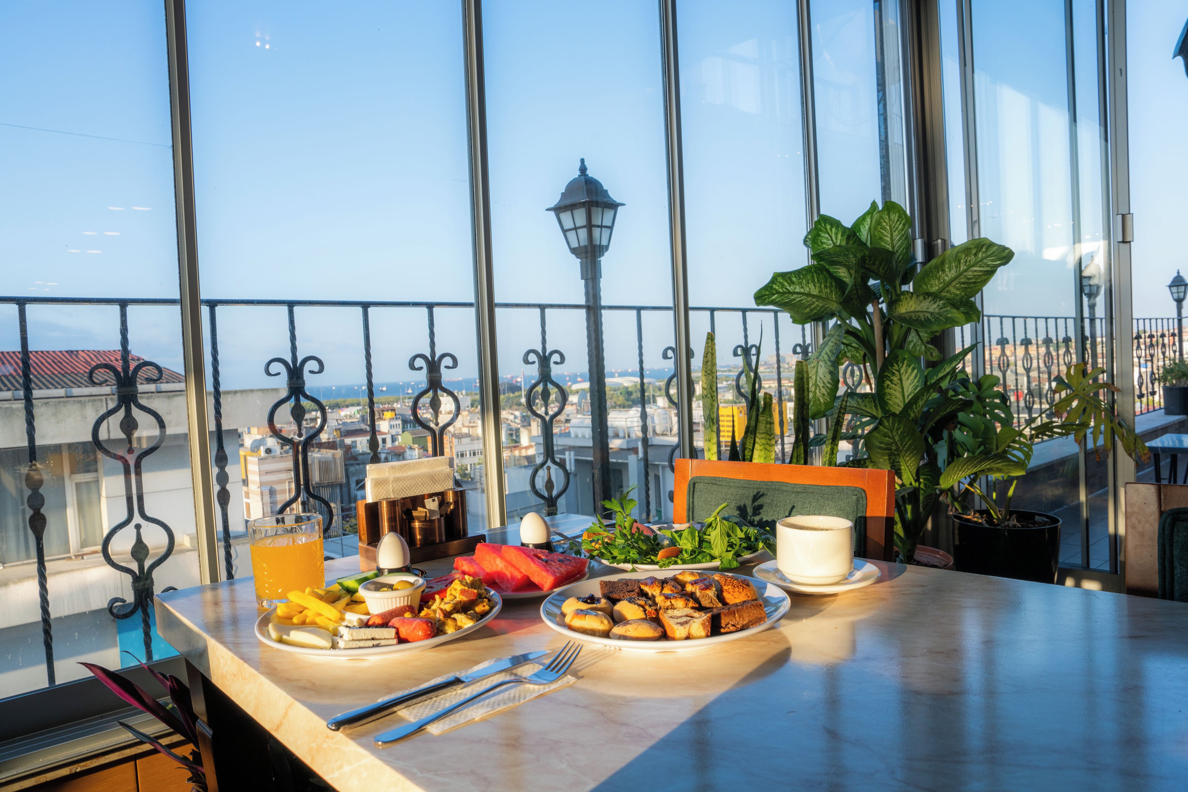 A dining table with breakfast items, a potted plant, and a view of the city through large windows.
