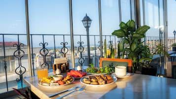 A dining table with breakfast items, a potted plant, and a view of the city through large windows.