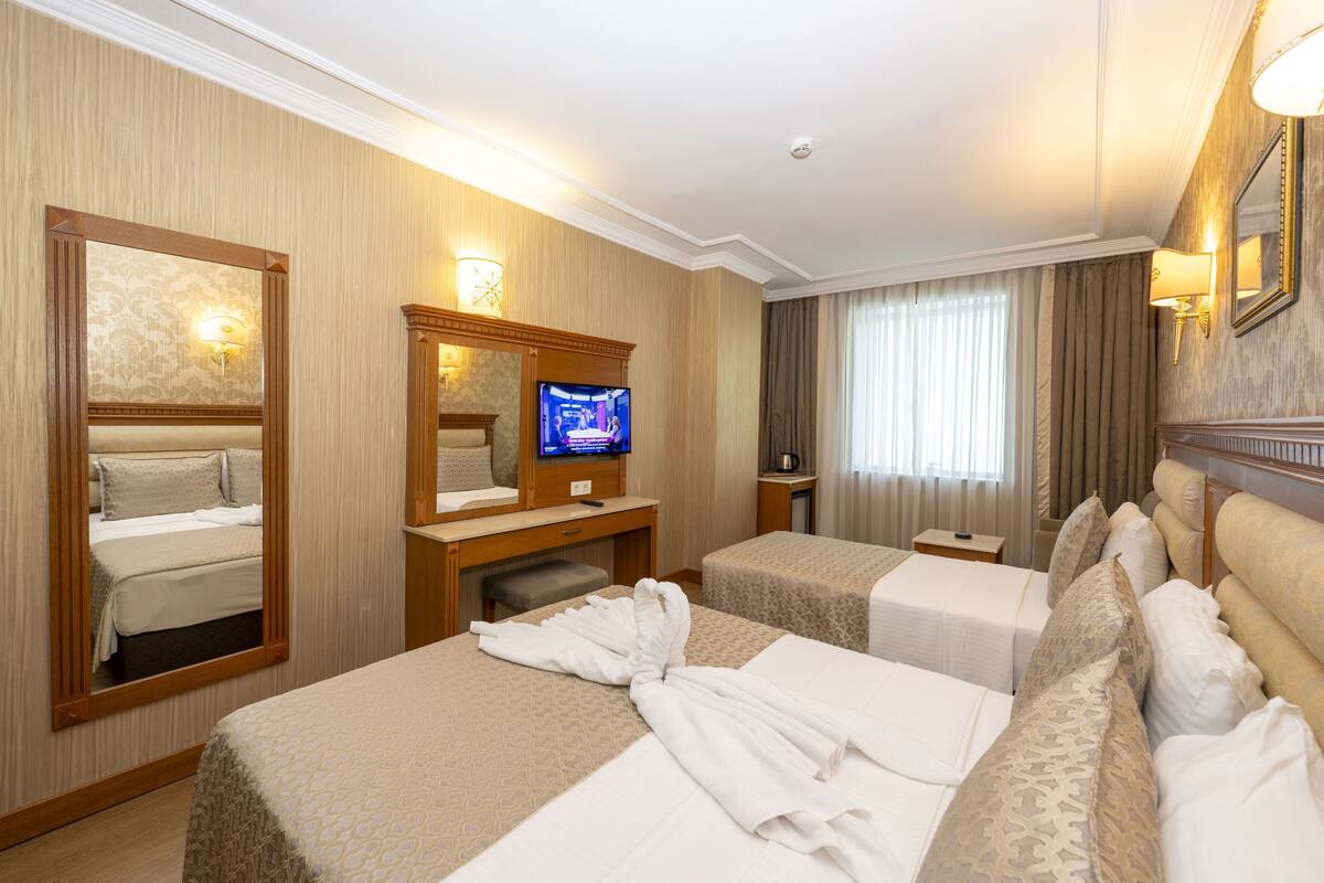 Une chambre d’hôtel avec deux lits, une télévision, un miroir et un bureau avec une lampe.