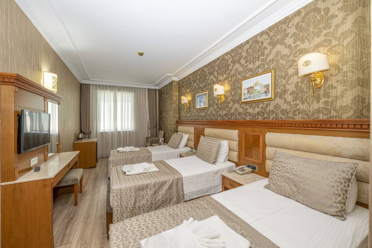 Une chambre d’hôtel avec trois lits, un bureau, une télévision et une salle de bain.