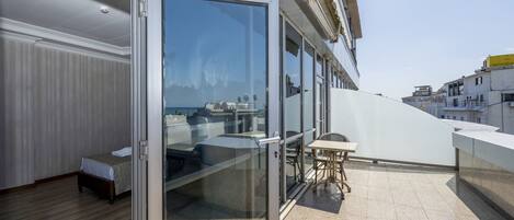 A balcony with a glass door, a bed, and a small table with chairs.