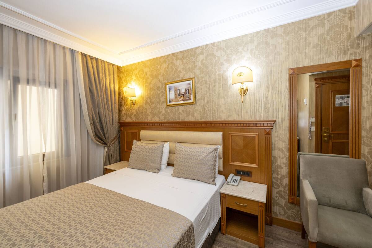 Une chambre d’hôtel avec un grand lit, deux lampes de chevet, un téléphone, une chaise et une porte.