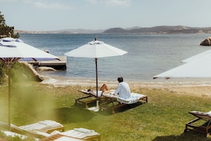 Uma área de estar à beira-mar com espreguiçadeiras e guarda-sóis, com vista para o mar.