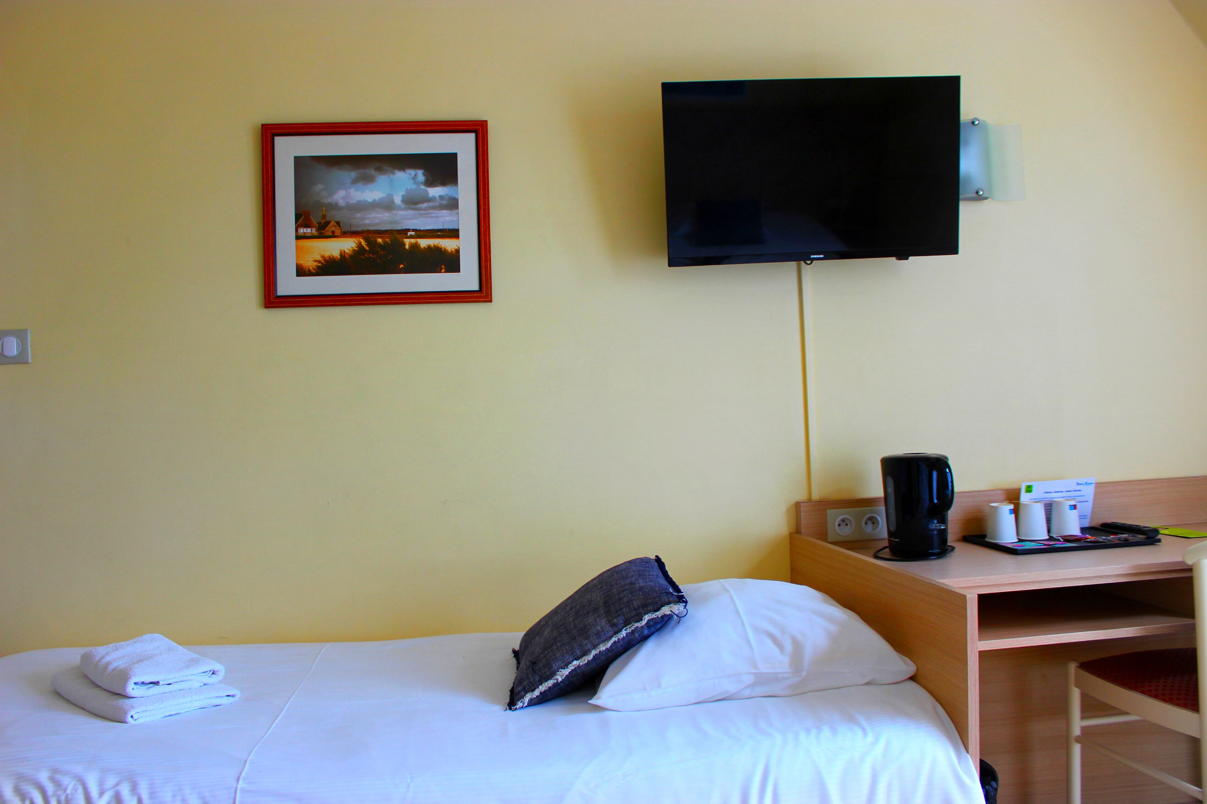 Hotellihuone, jossa on sänky, työpöytä, televisio ja seinällä kehystetty taulu.