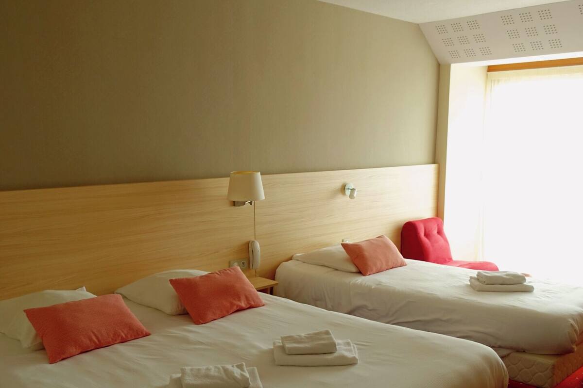 Habitación de hotel con dos camas, cada una con sábanas blancas y almohadas rojas. Se observan toallas dobladas sobre cada cama.