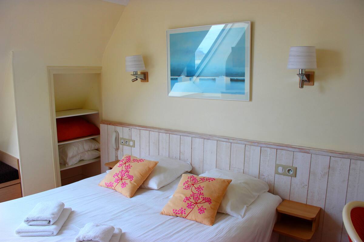 Una habitación de hotel con una cama, dos lámparas de noche, un cuadro y una silla roja.