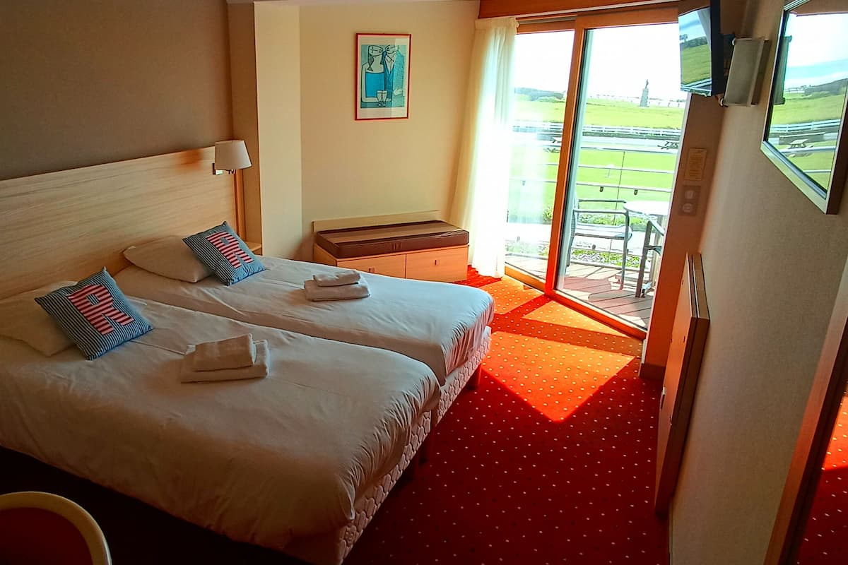 Habitación de hotel con dos camas, una mesita, una silla y vistas al exterior.