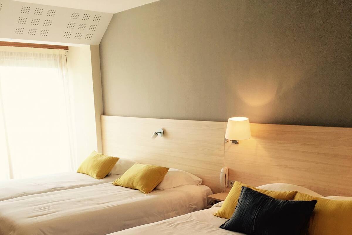 Habitación de hotel con dos camas, cada una con cabecero y lámpara de noche.
