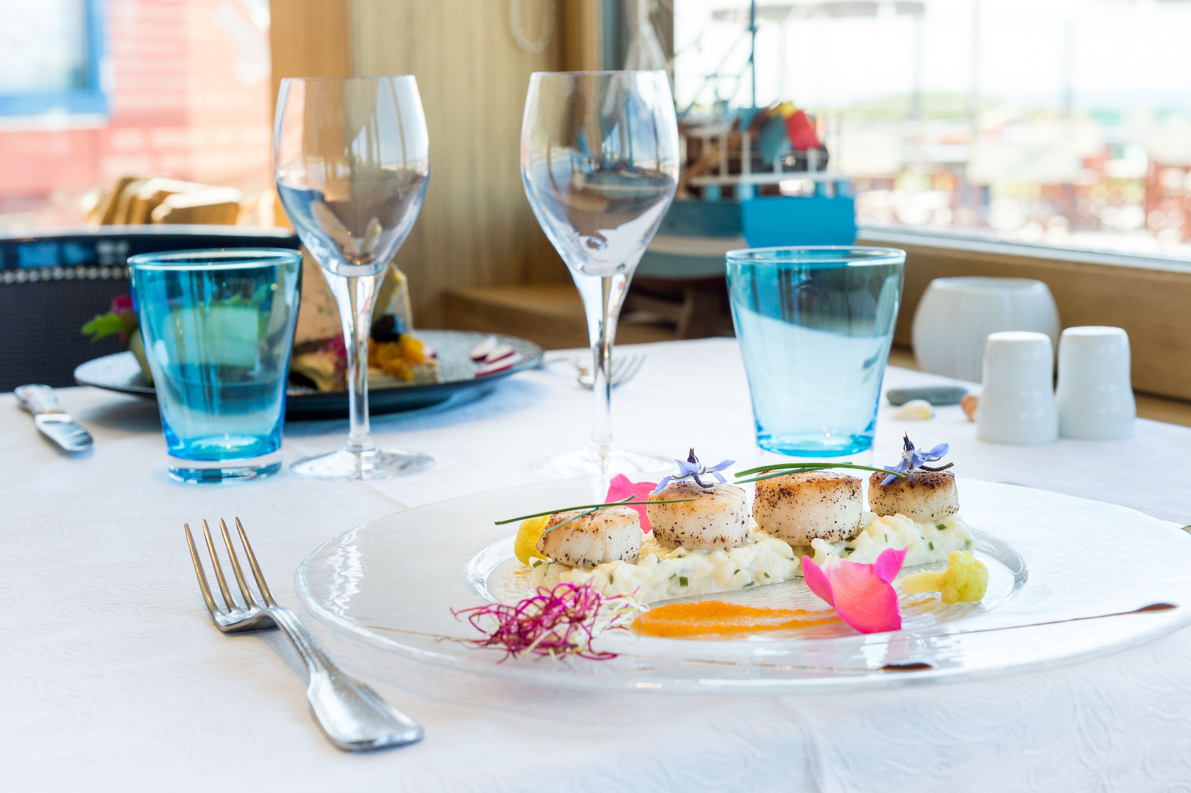 A dining table with a seafood dish, wine glasses, and a view of the city.