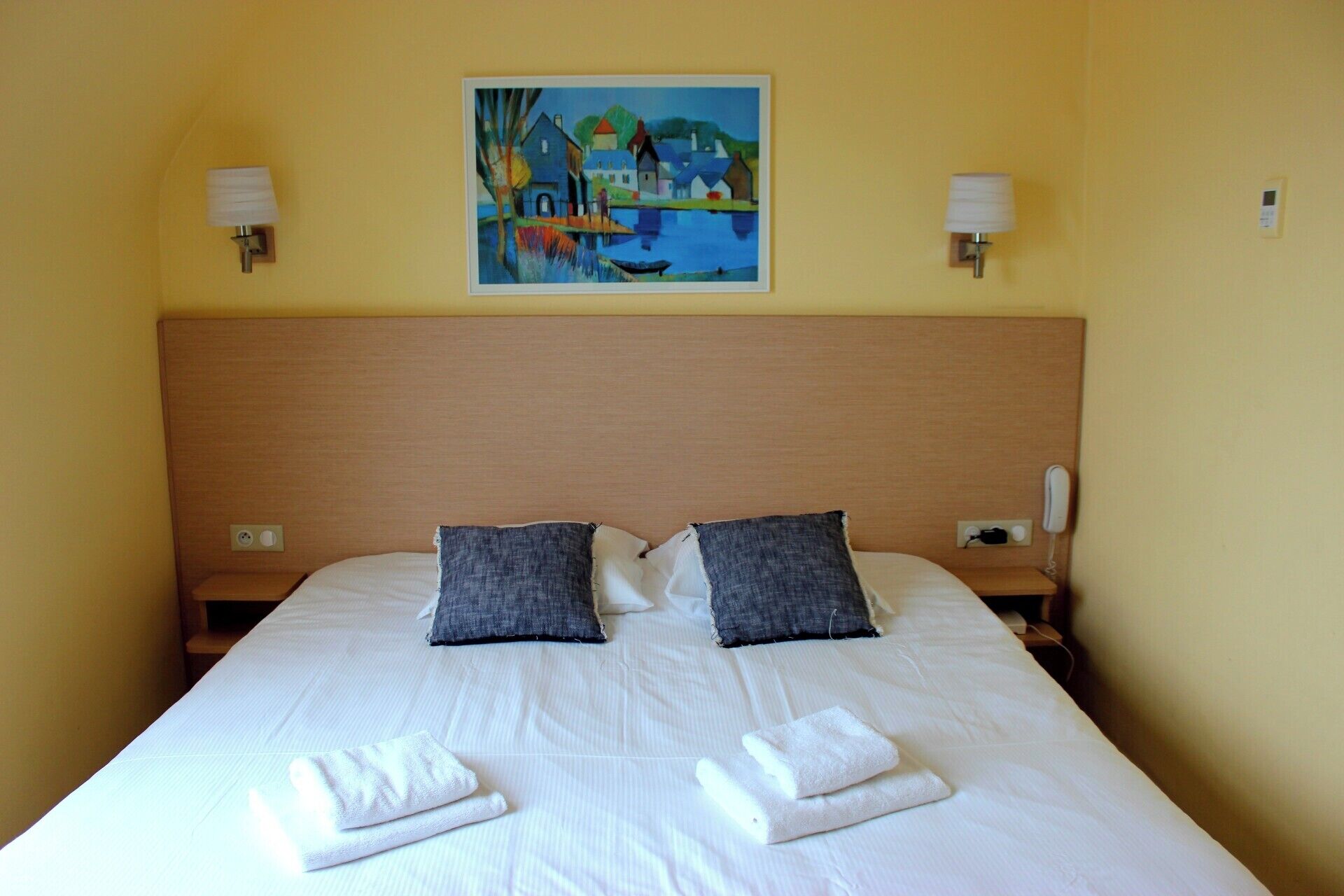 Une chambre d’hôtel avec un grand lit, deux oreillers, un tableau au mur et un téléphone sur la table de chevet.