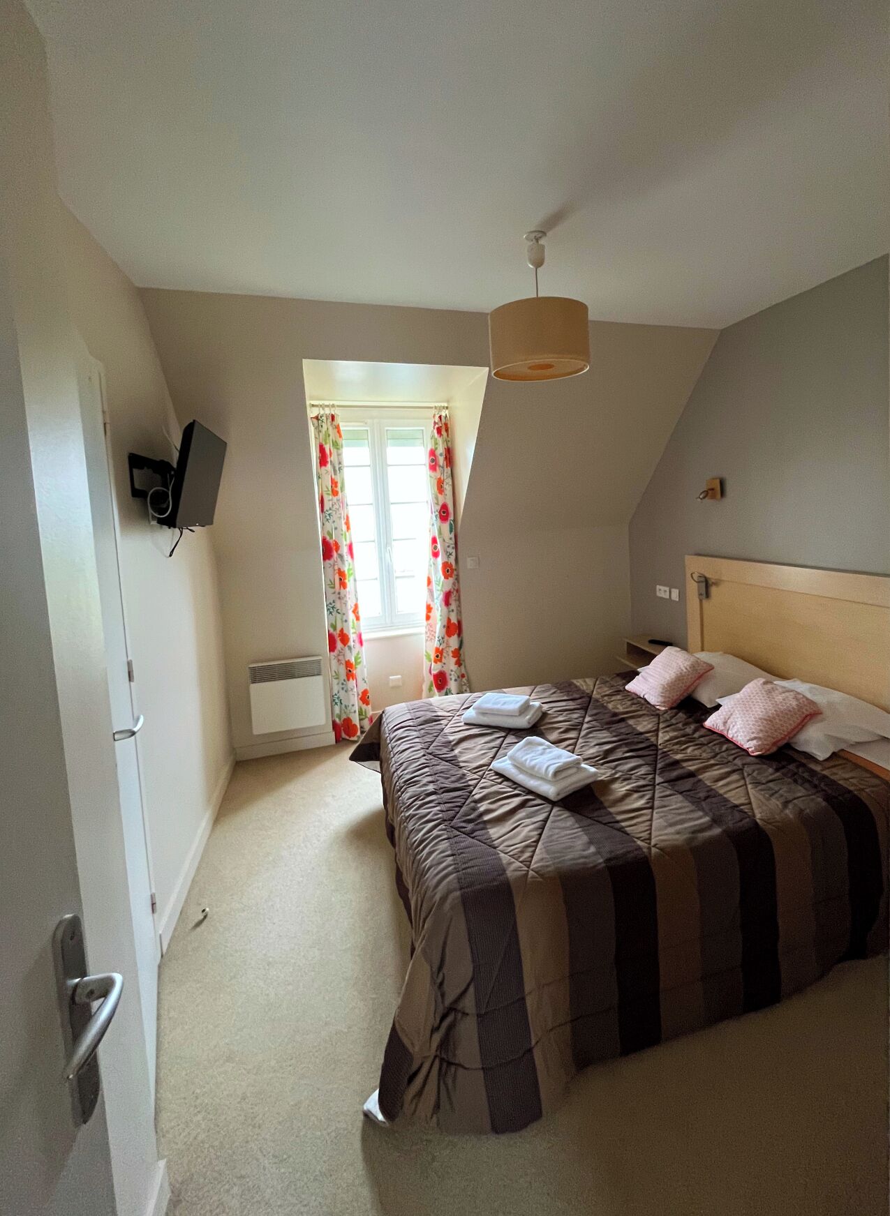 Un dormitorio con cama, televisor, ventana con cortinas y ventilador de techo.