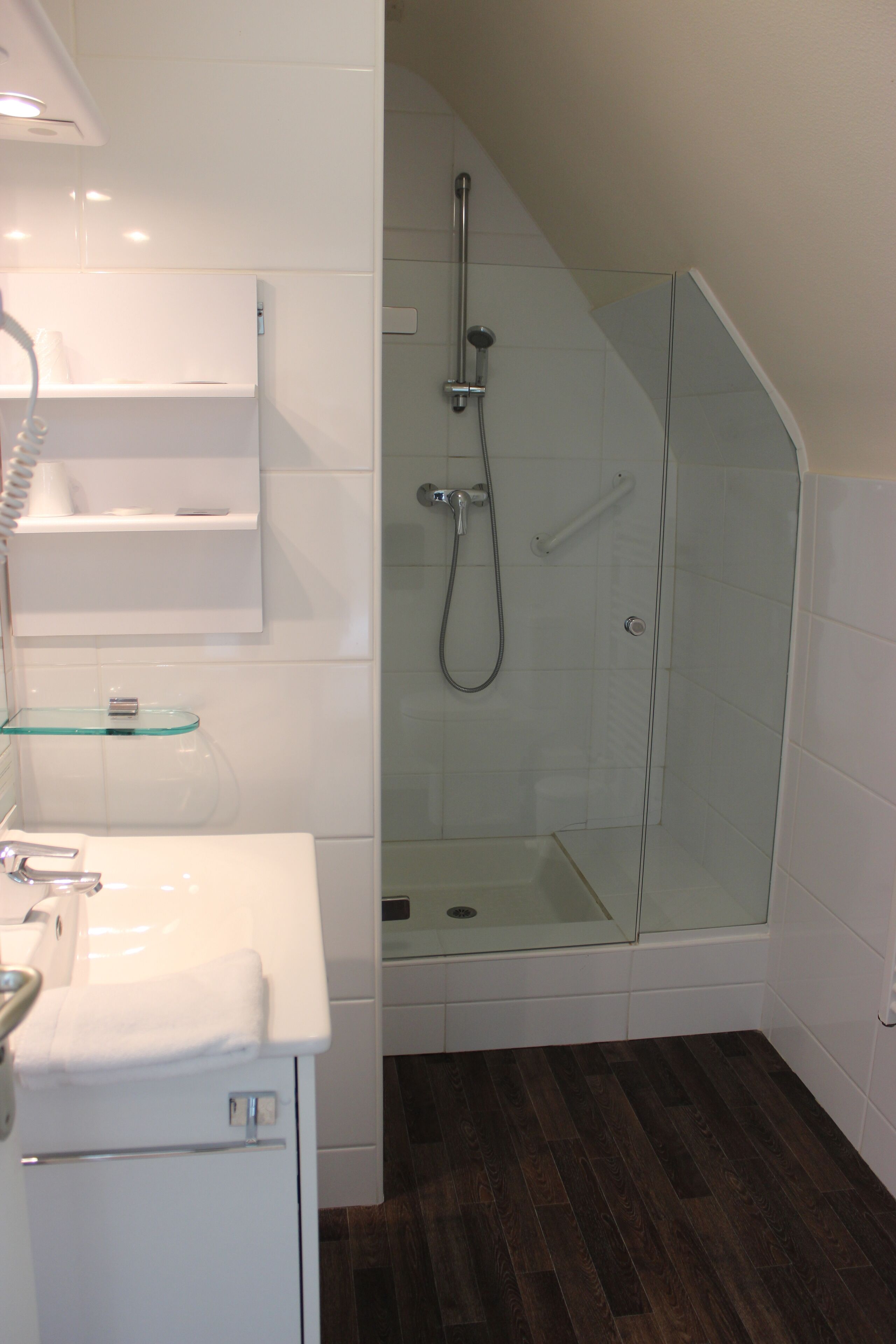 Un baño moderno con ducha acristalada, azulejos blancos y suelo de madera.