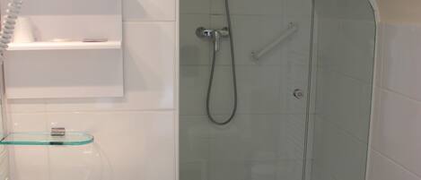 Un baño moderno con ducha acristalada, azulejos blancos y suelo de madera.