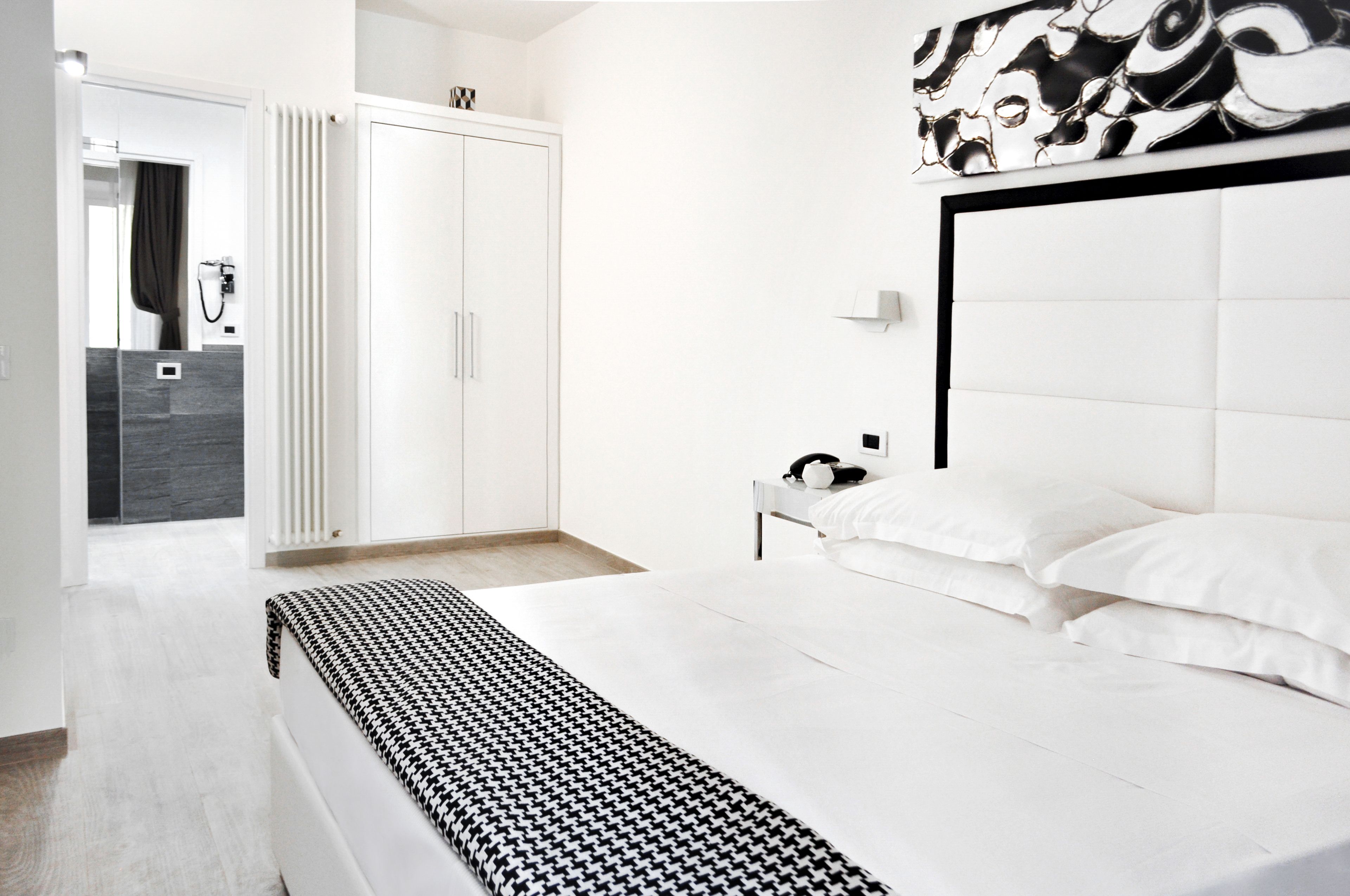 A modern hotel room with a large bed, a wardrobe, a bathroom with a shower, and a decorative wall piece.