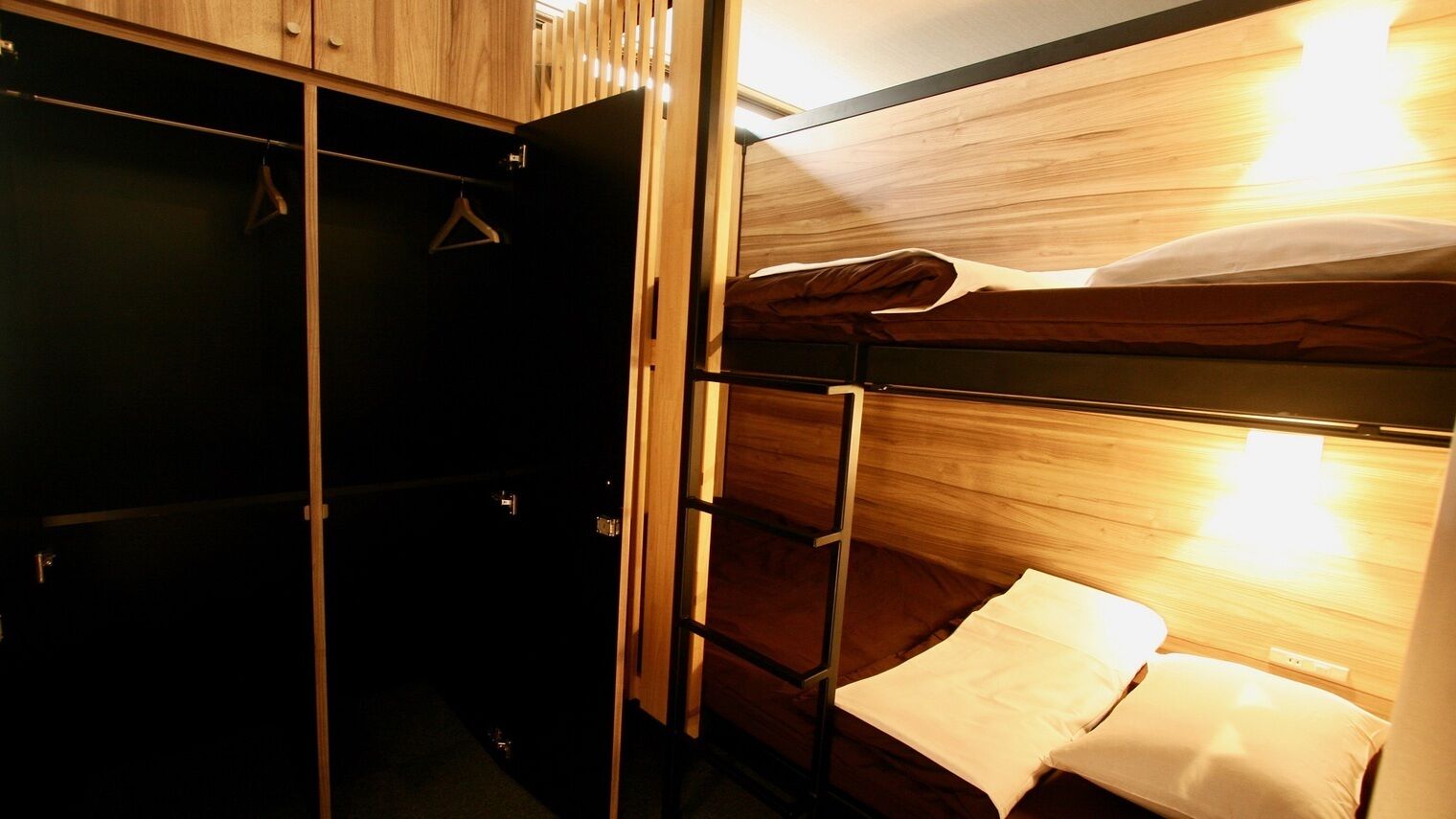 Ein Stockbett mit einem hölzernen Kopfteil, einem Kleiderhaken und einer kleinen Ablagefläche.