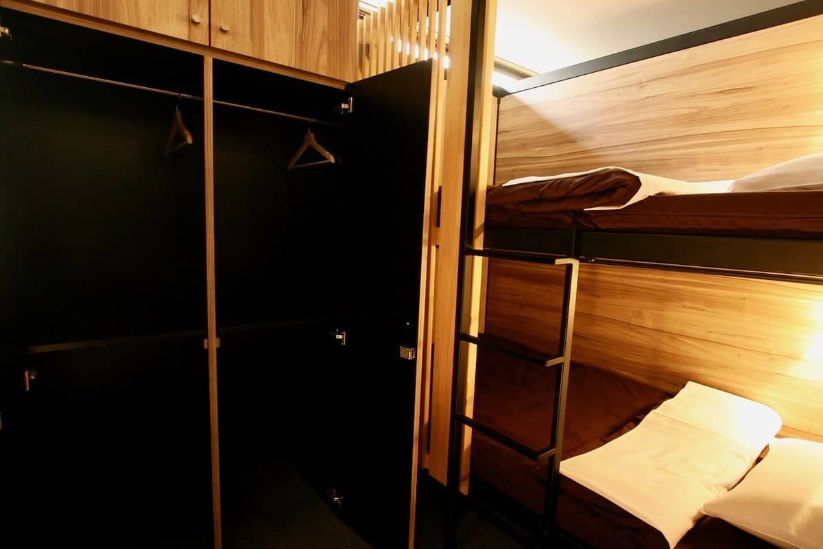 Ein Stockbett mit einem hölzernen Kopfteil, einem Kleiderhaken und einer kleinen Ablagefläche.