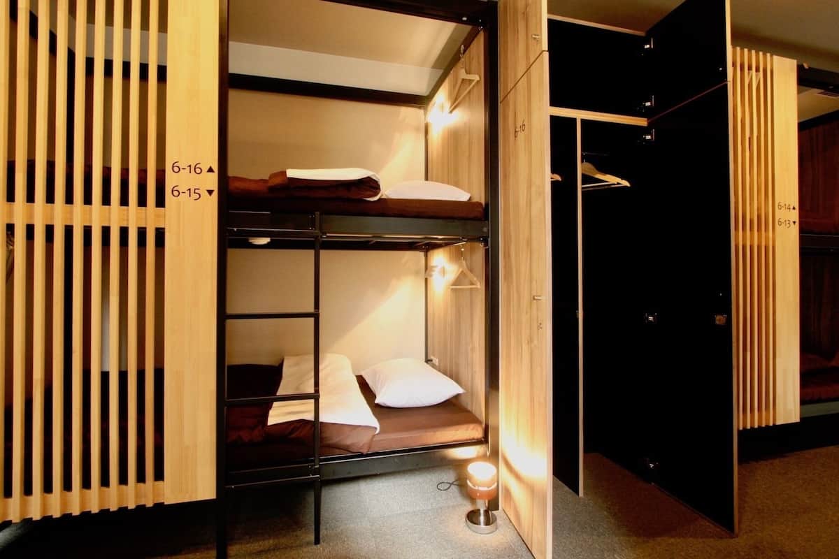 A bunk bed room with wooden slats, a bedside lamp, and a hanging coat rack.