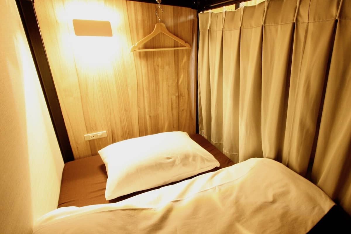 A single bed with a white pillow and a wooden headboard, a hanging garment rack, and beige curtains.