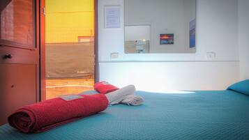 A room with a bed, a window, a door, and a wall-mounted mirror.