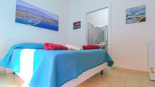 Un dormitorio con cama, un ventanal grande y un cuadro de una escena costera.