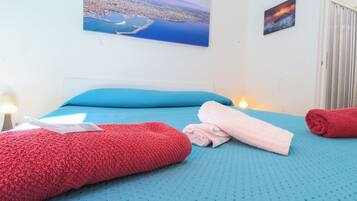 Habitación de hotel con cama, ropa de cama azul, una toalla roja y una toalla blanca, junto con un cuadro de un paisaje costero.