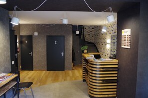 A reception area with a wooden reception desk, a black door, and a staircase with patterned wallpaper. - Le Chêne Vert (Savenay)
