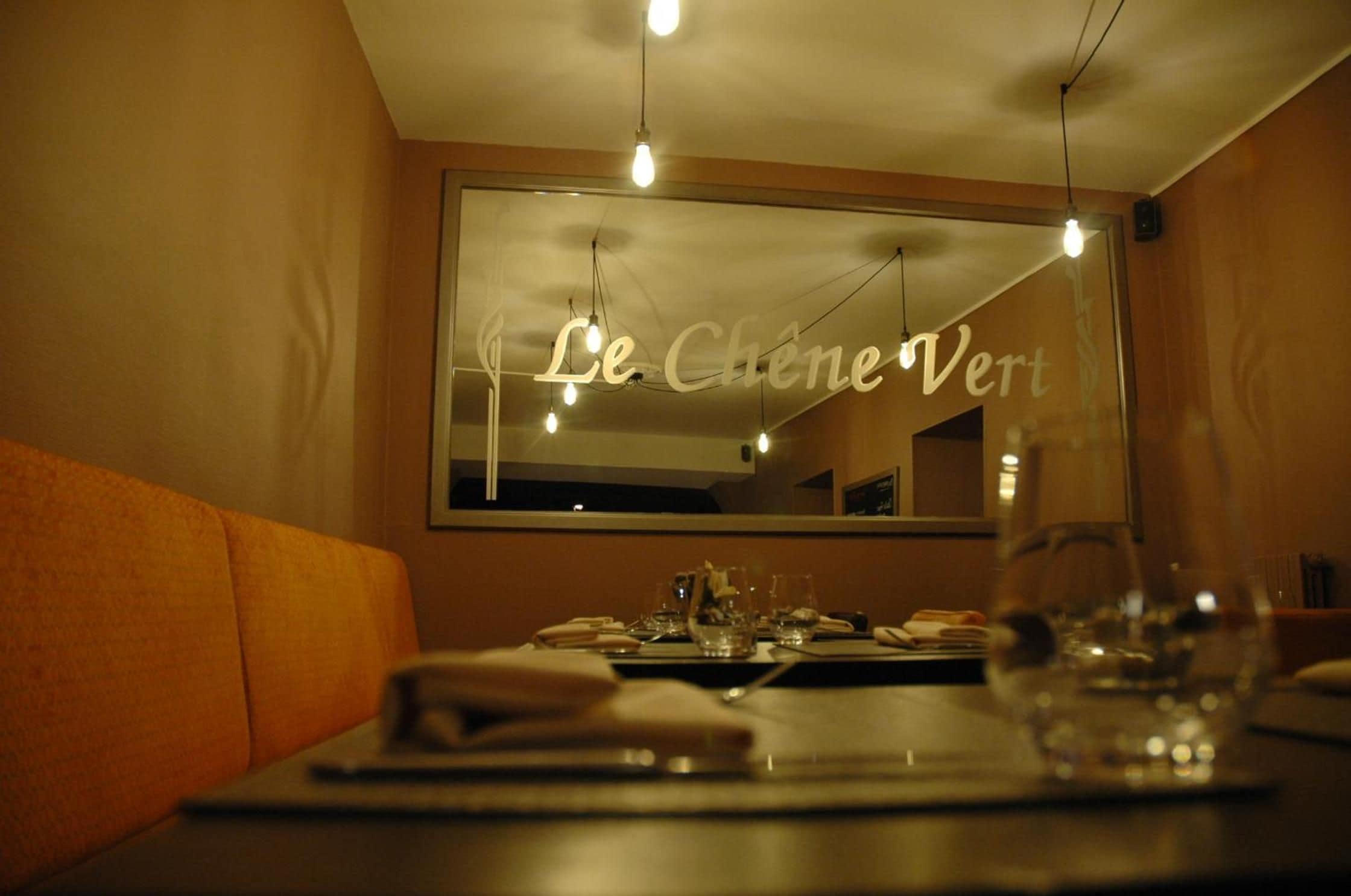 L'intérieur d'un restaurant, avec une table dressée pour deux personnes, un grand miroir au mur et une enseigne indiquant « Le Chêne Vert ».