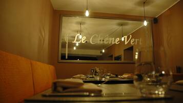 L'intérieur d'un restaurant, avec une table dressée pour deux personnes, un grand miroir au mur et une enseigne indiquant « Le Chêne Vert ».