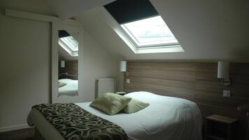 A bedroom with a skylight, a bed with a patterned bedspread, a bedside table, and a mirror.