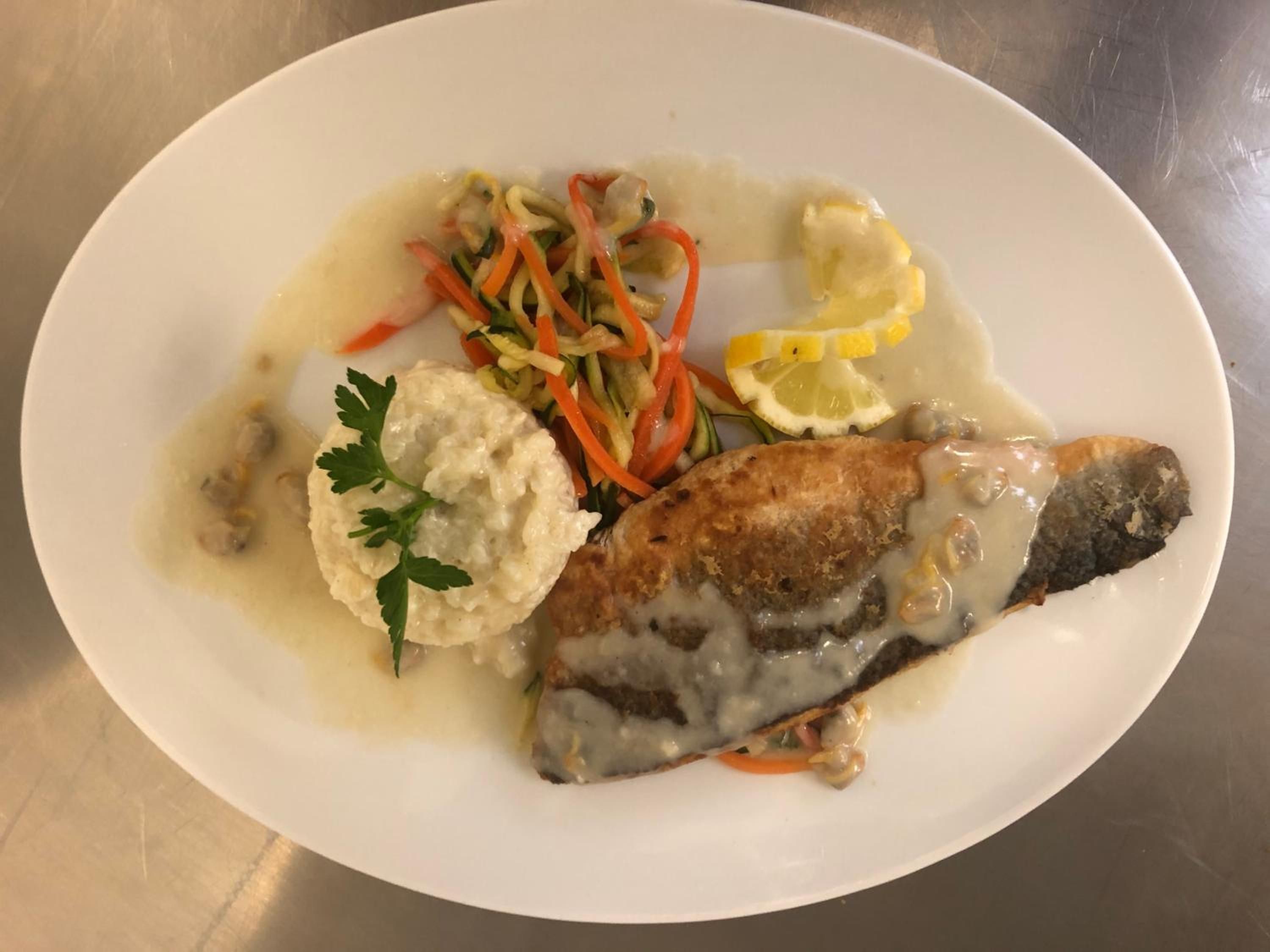 Un plato con un filete de pescado, puré de papas y una ensalada de verduras.