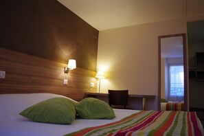 A hotel room with a bed, two green pillows, a striped blanket, a desk with a chair, and a lamp. - Le Chêne Vert (Savenay)
