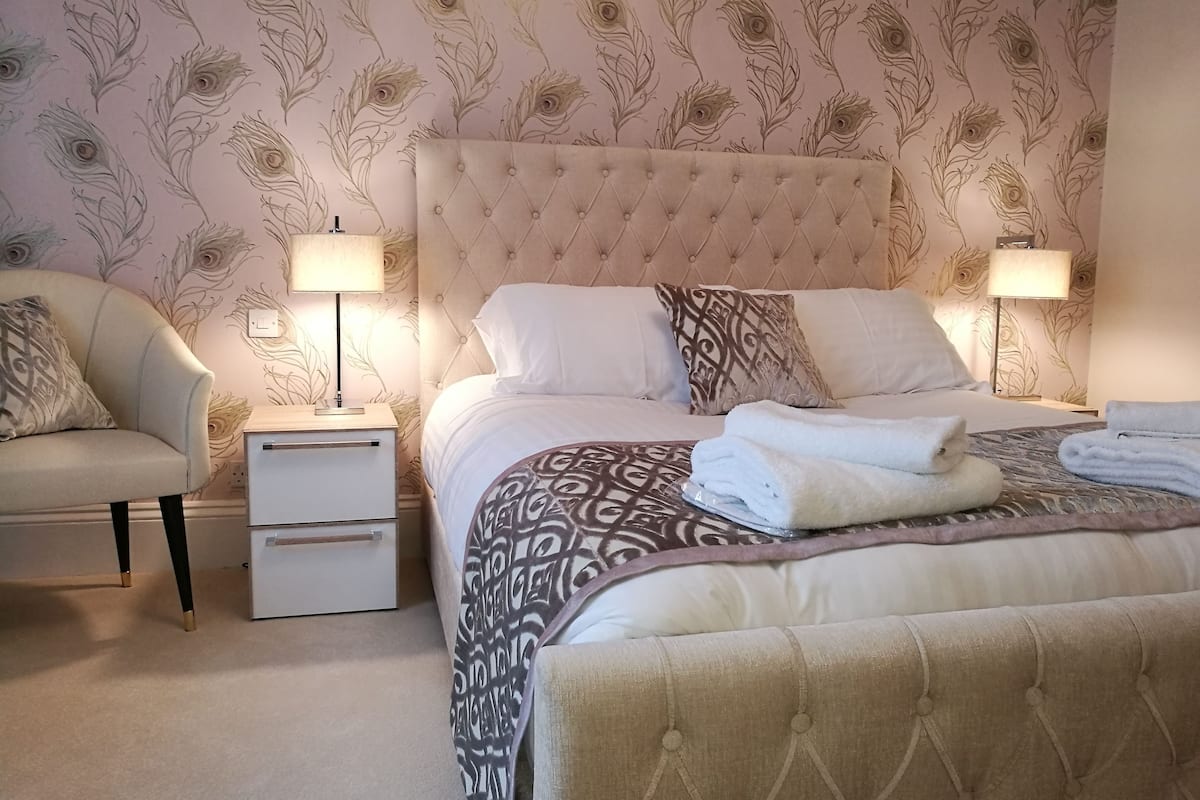 A bedroom with a tufted headboard, two bedside tables with lamps, a bed with patterned bedding, and a chair.